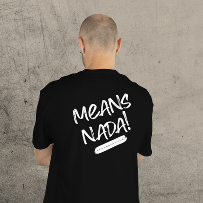 Person wearing a black t-shirt with 'MEANS NADA!' text on the back against a gray concrete wall.