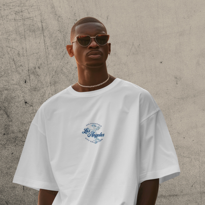 Man wearing a white t-shirt with a 'Los Angeles' logo against a textured wall.
