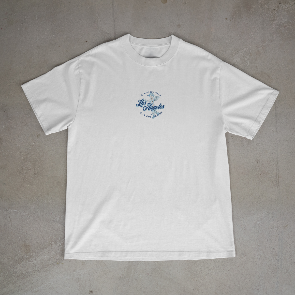White t-shirt with blue graphic on a gray concrete surface
